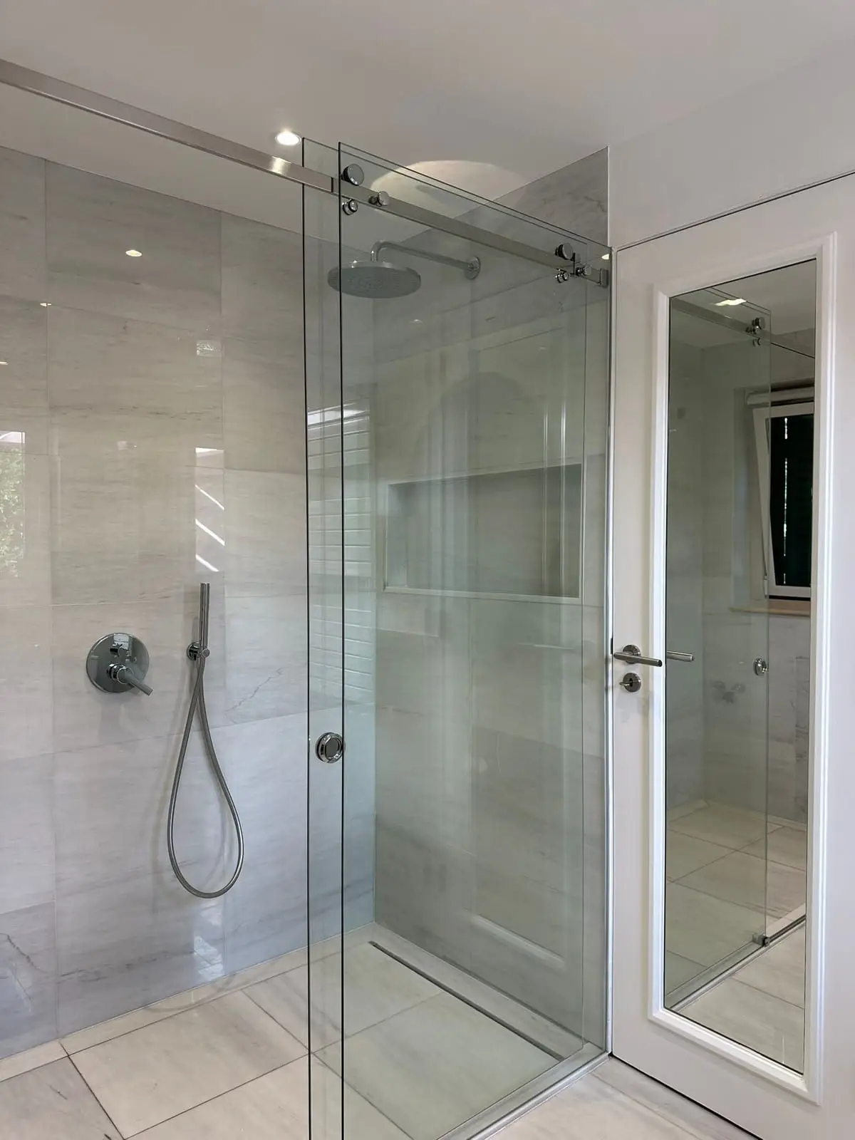 The finished shower in grey marble-look porcelain behind a frameless glass screen, with a ceiling rain head