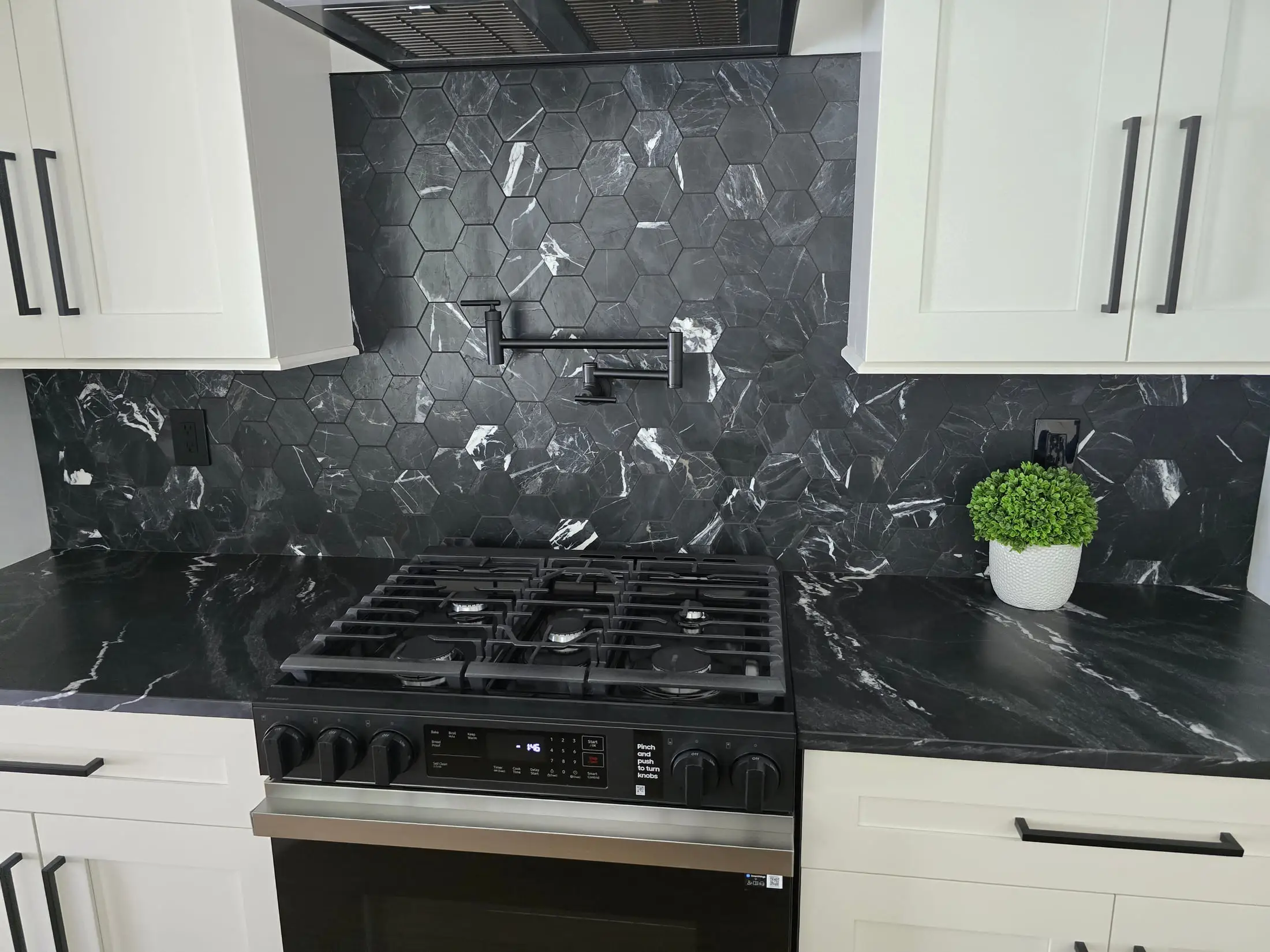 Kitchen backsplash in black marble with heavy white veining, cut around a gas cooktop and pot filler