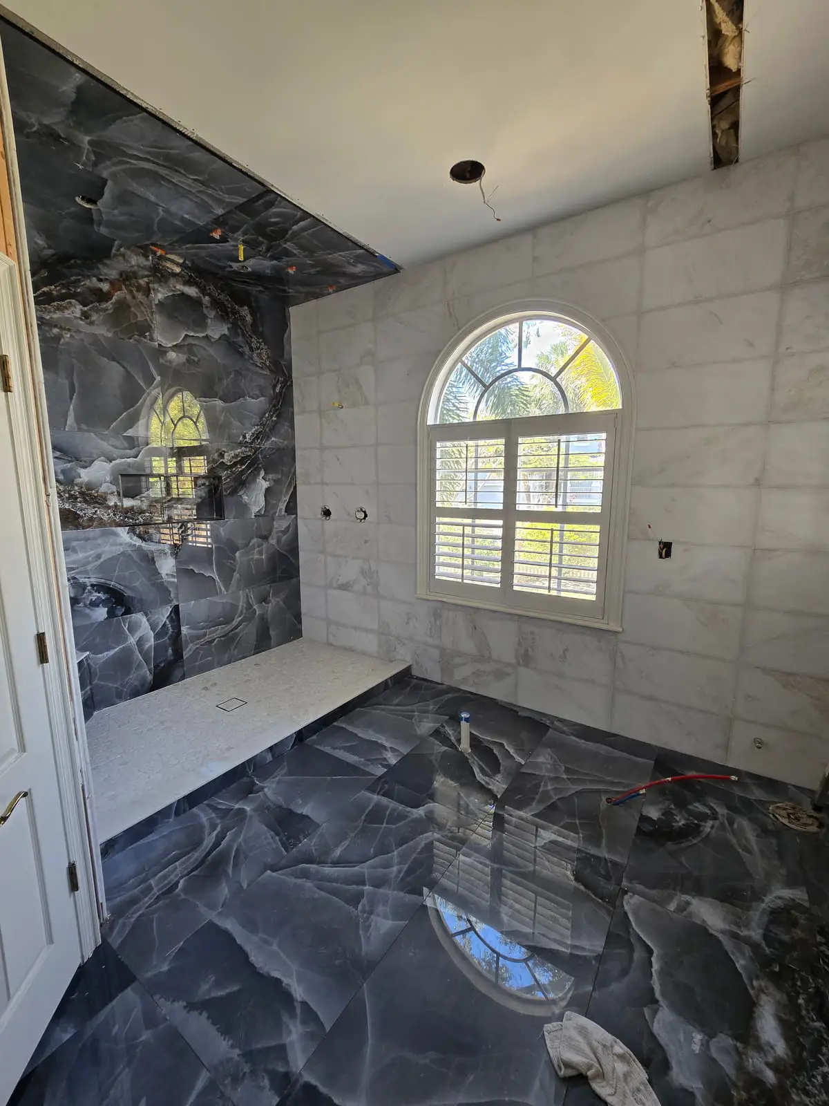 Shower with a black marble-look feature wall and a white mosaic bench, opening onto the finished black marble floor