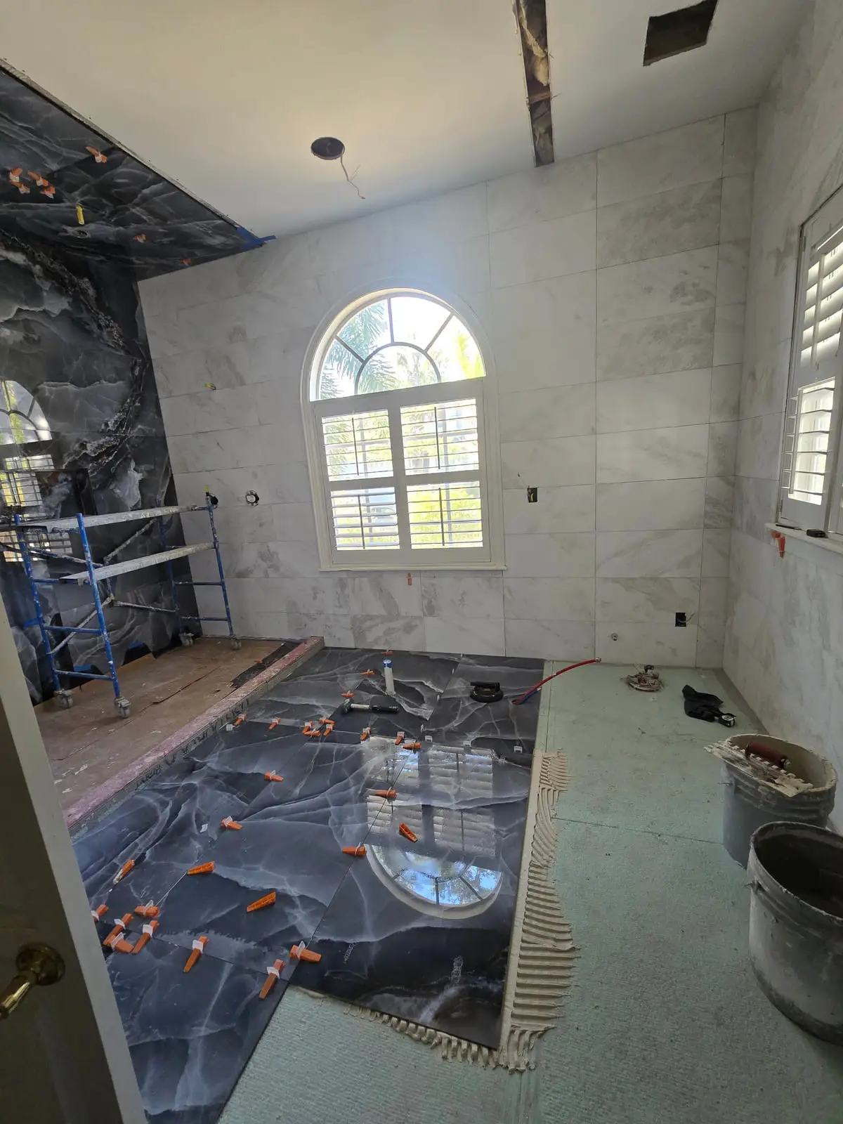 Large black marble-look floor tiles being laid with levelling clips in place, against walls already finished in white marble-look porcelain