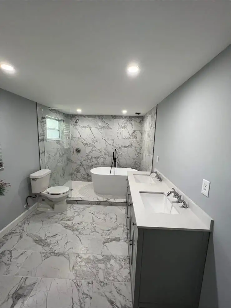Bathroom finished in marble-look porcelain with a freestanding tub set on a mosaic platform and a grey double vanity opposite