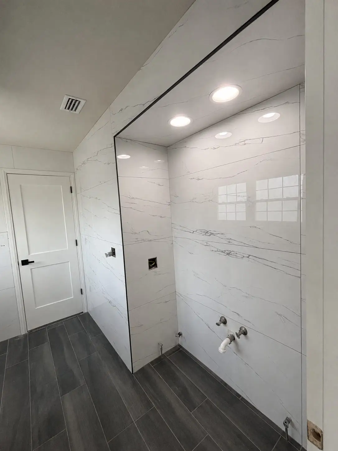 Walk-in shower lined in marble-look porcelain with a frameless glass panel, set against a dark plank floor