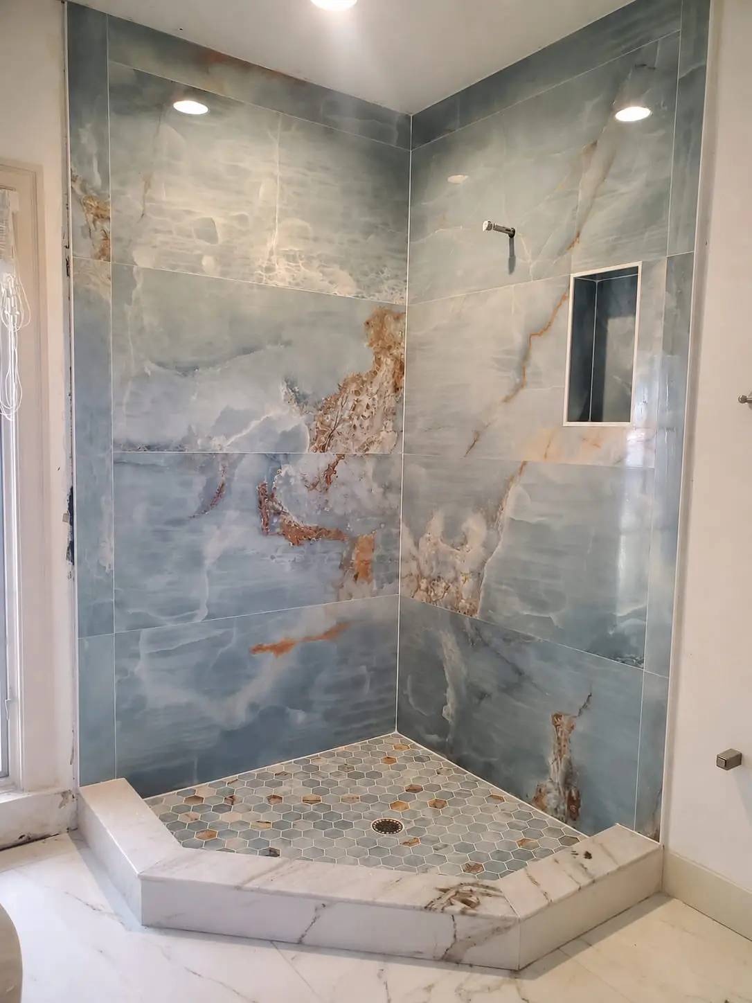 Corner shower clad floor to ceiling in blue onyx-look porcelain with amber veining carried across the joints, over a mosaic shower floor