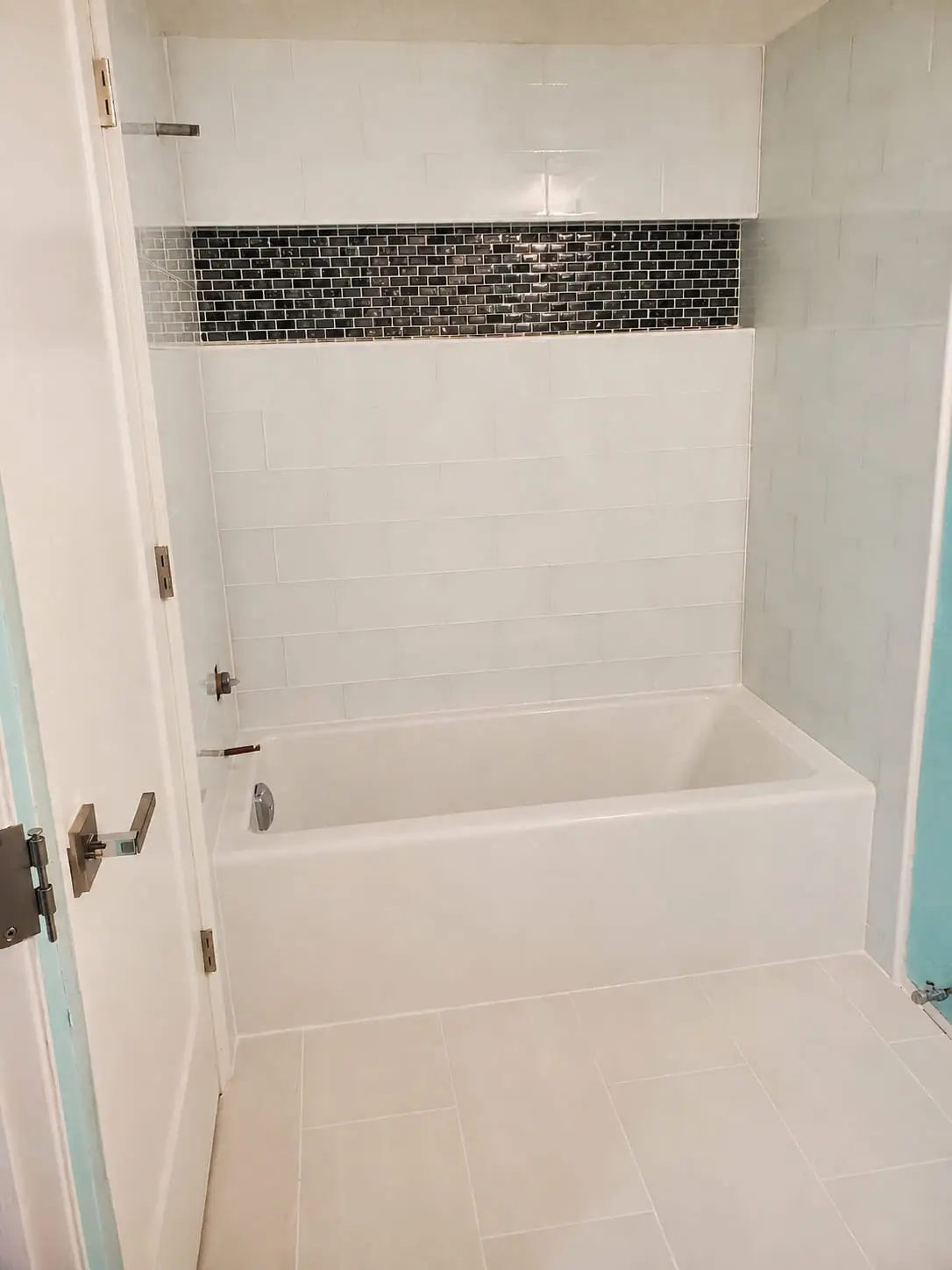 Built-in tub with a dark mosaic band set into the surrounding wall tile as a recessed shelf