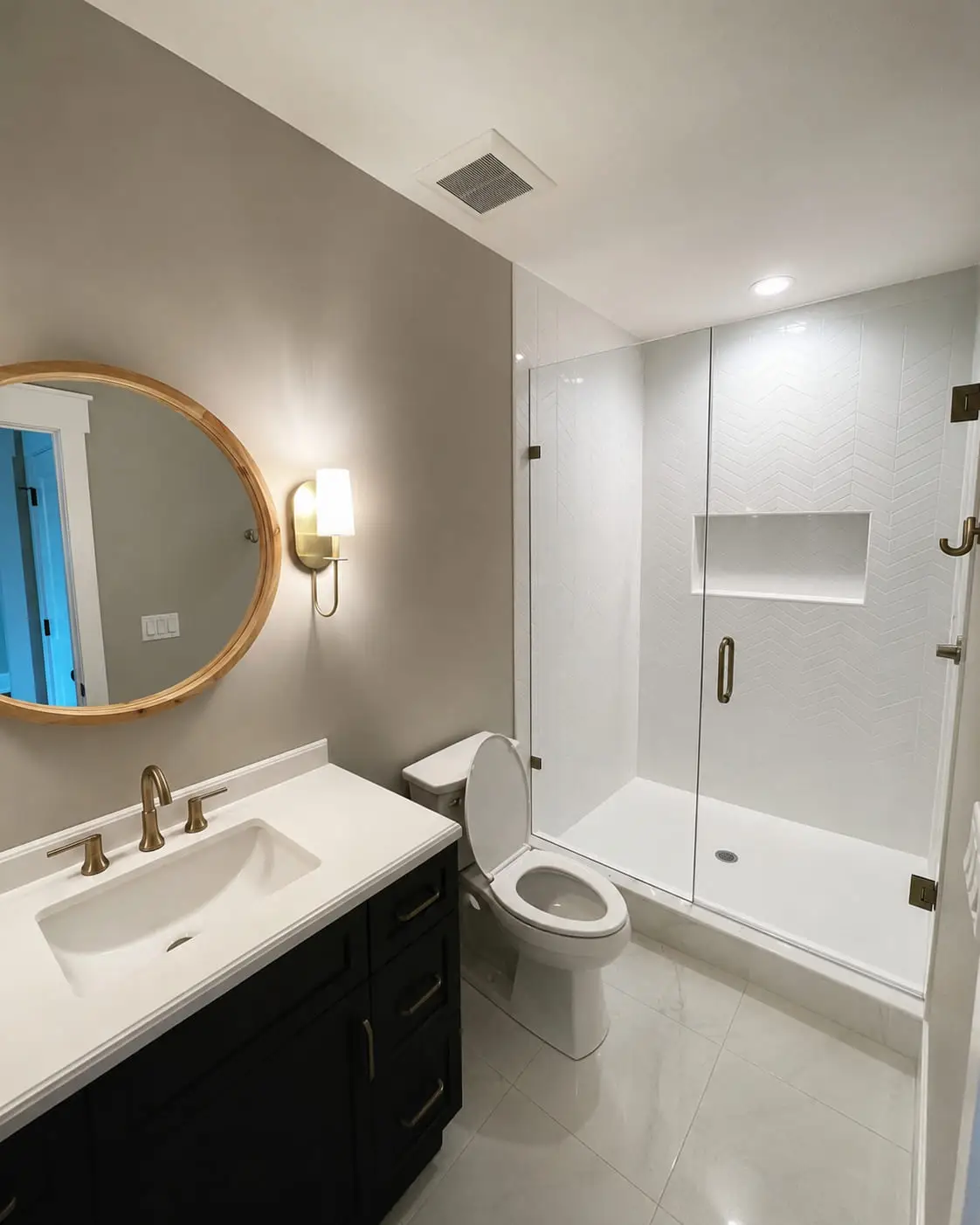 Completed bathroom remodel with a dark vanity, round mirror, brass tapware and a frameless glass shower
