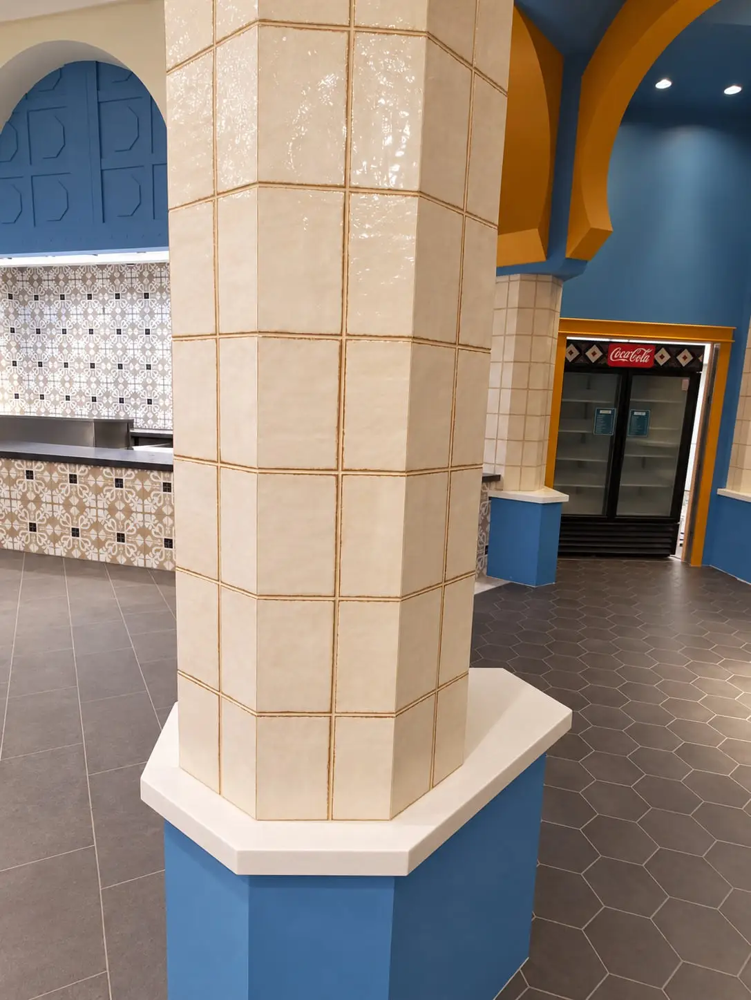 Structural column wrapped in cream glazed tile with a stone cap, set on a hexagonal tile floor