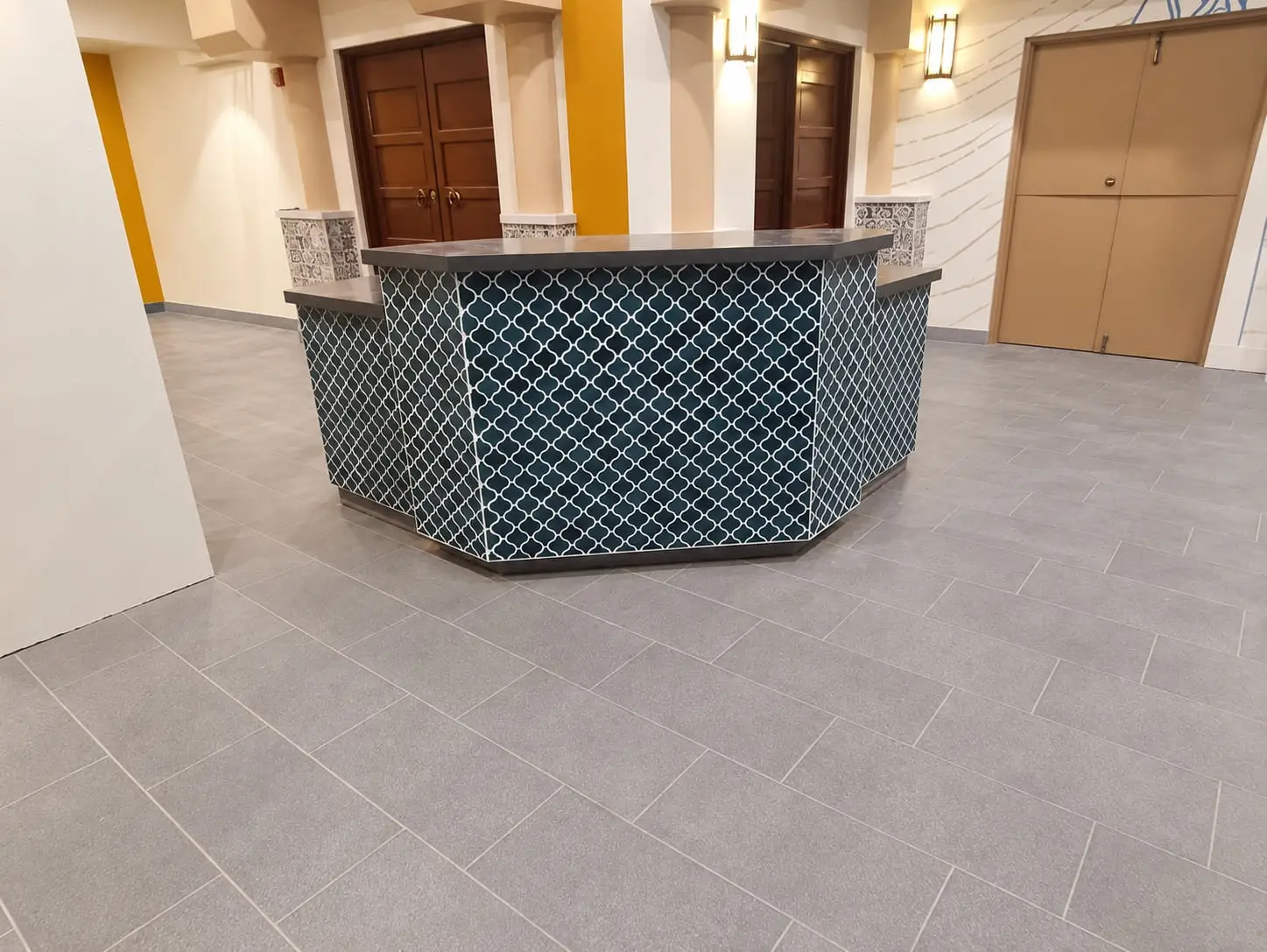Angled reception desk clad in blue arabesque tile, standing on a large-format grey floor