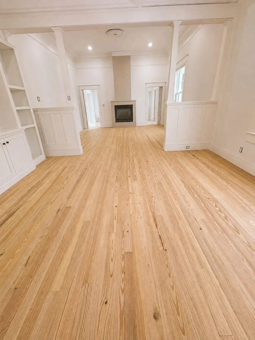 Wide-plank wood floor running the length of a living room, carried straight past a built-in fireplace and its joinery without a break