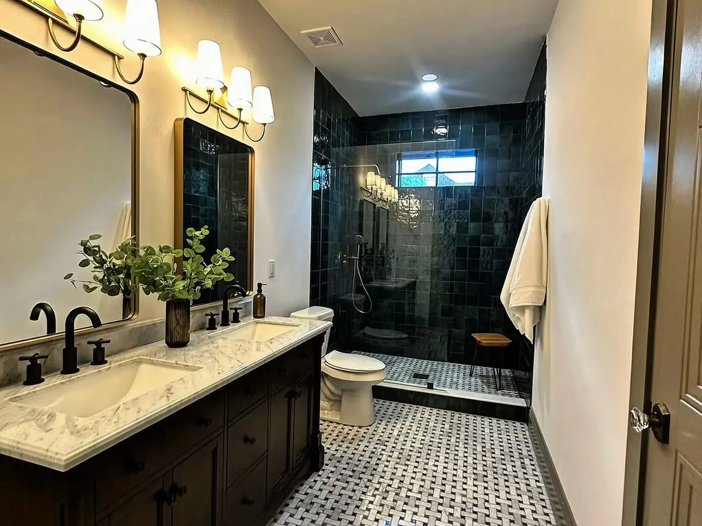 Bathroom with a green tiled shower, a dark double vanity and a basketweave marble floor, by General Tile Company