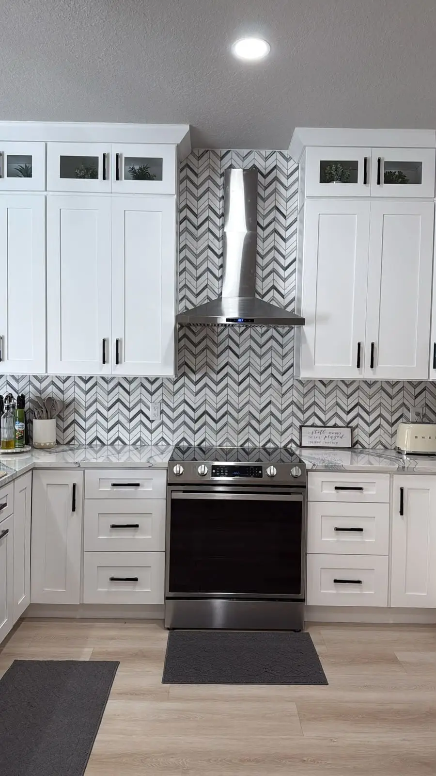 White shaker kitchen with a chevron marble mosaic backsplash carried up the wall and around the range hood, by General Tile Company