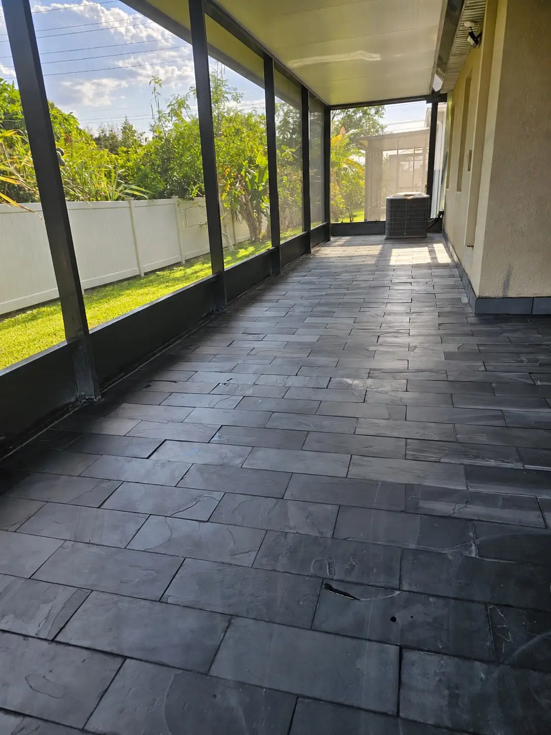 Screened lanai floored in dark slate-look plank tile, running the length of the enclosure