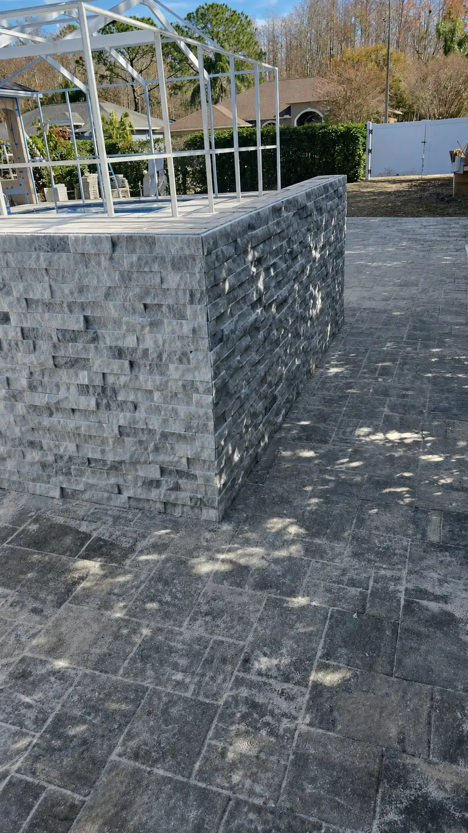 Pool deck in a French-pattern paver layout beside a low wall clad in grey stacked stone ledger
