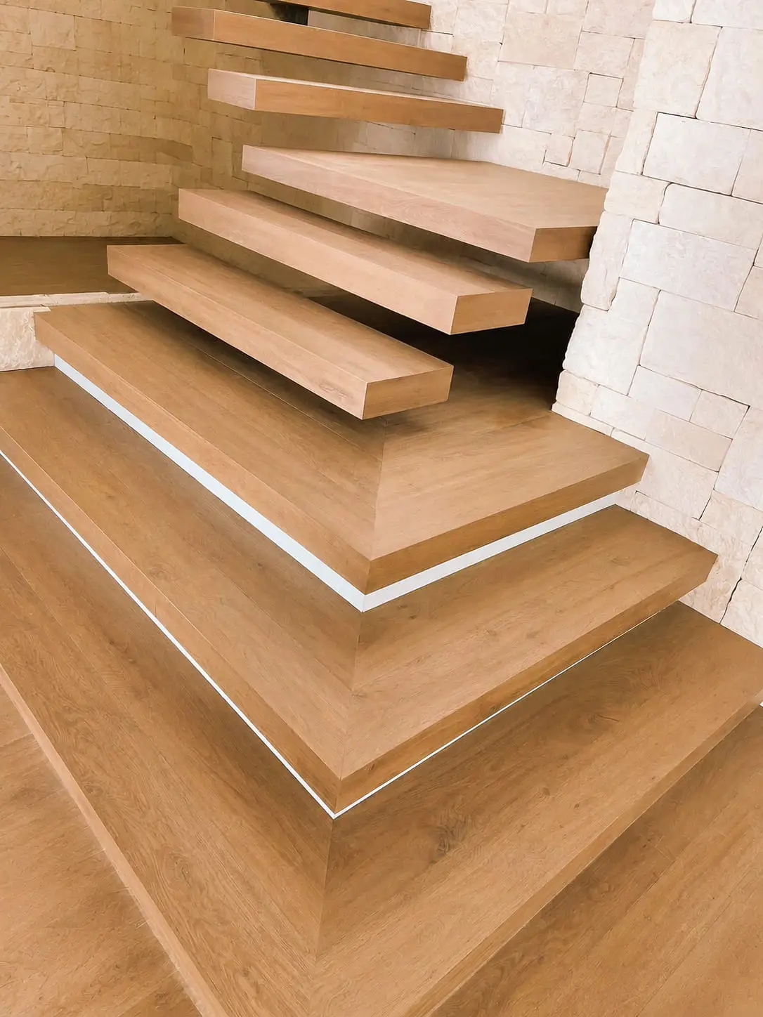Floating oak stair treads cantilevered from a rustic stone wall, each nosing aligned to the one below